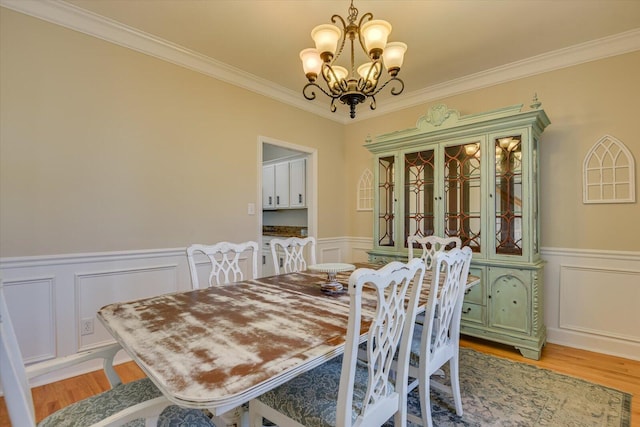 dining area with wainscoting, crown molding, light wood-style flooring, and an inviting chandelier