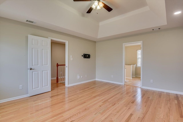 unfurnished bedroom featuring a tray ceiling, visible vents, light wood-style flooring, and baseboards