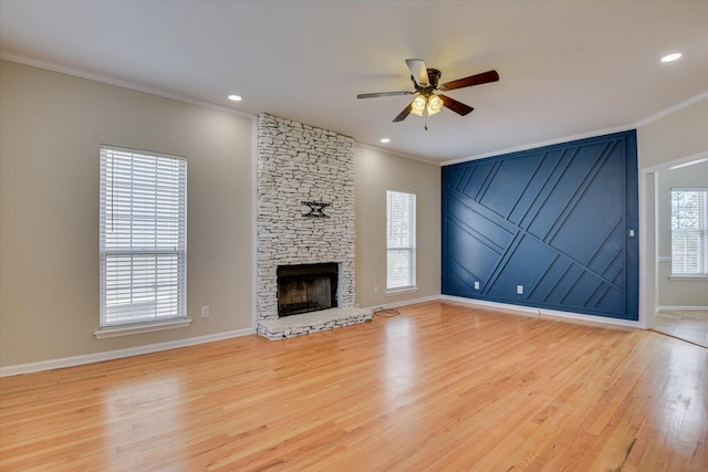 unfurnished living room featuring baseboards, ceiling fan, wood finished floors, crown molding, and a stone fireplace