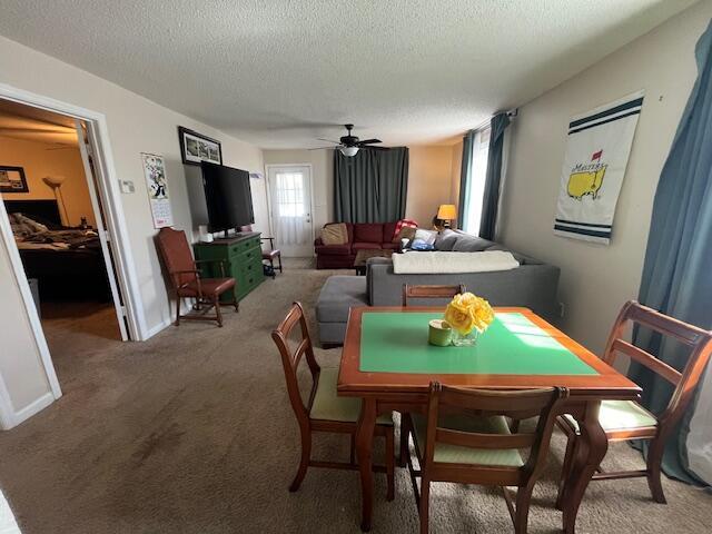 dining room featuring a textured ceiling, light carpet, baseboards, and ceiling fan