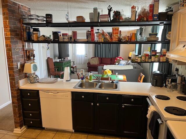 kitchen with a sink, dark cabinetry, white appliances, light countertops, and light tile patterned floors