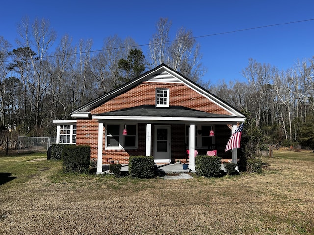 view of front facade featuring a front yard, fence, brick siding, and covered porch