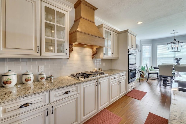 kitchen featuring backsplash, premium range hood, ornamental molding, decorative light fixtures, and stainless steel appliances