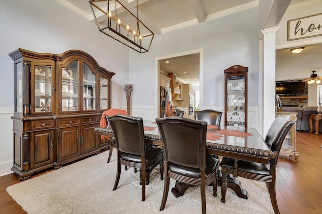 dining space featuring hardwood / wood-style floors, ceiling fan with notable chandelier, and decorative columns