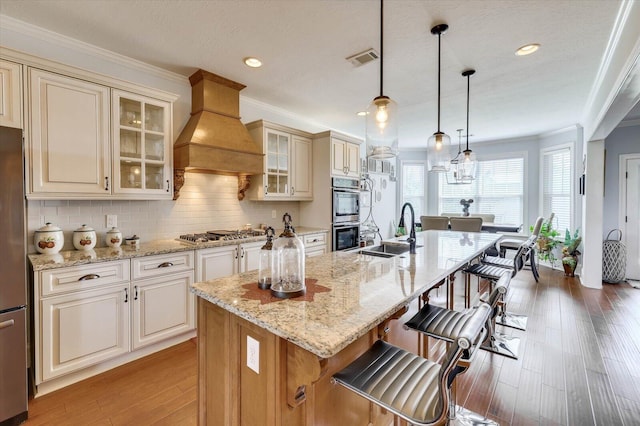 kitchen with a center island with sink, hanging light fixtures, custom range hood, and sink