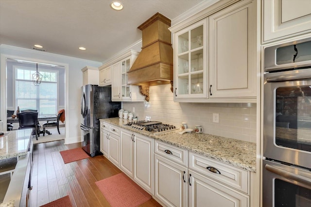 kitchen with pendant lighting, custom exhaust hood, crown molding, decorative backsplash, and stainless steel appliances