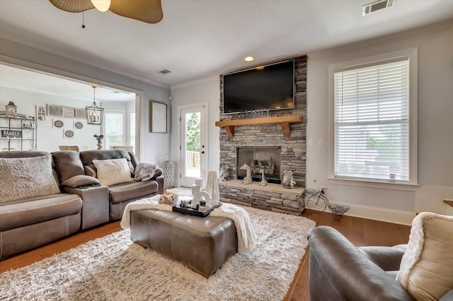 living room with a stone fireplace, a wealth of natural light, ornamental molding, and hardwood / wood-style flooring