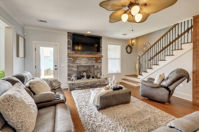 living room featuring a stone fireplace, crown molding, ceiling fan, and hardwood / wood-style flooring