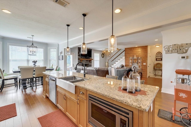 kitchen featuring appliances with stainless steel finishes, ornamental molding, sink, hanging light fixtures, and an island with sink