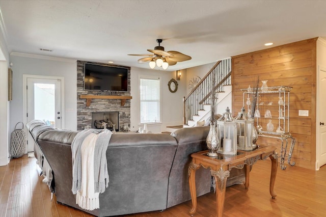 living room featuring a stone fireplace, ceiling fan, wood-type flooring, and ornamental molding