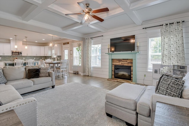 living room with ceiling fan, coffered ceiling, light hardwood / wood-style flooring, beamed ceiling, and a fireplace