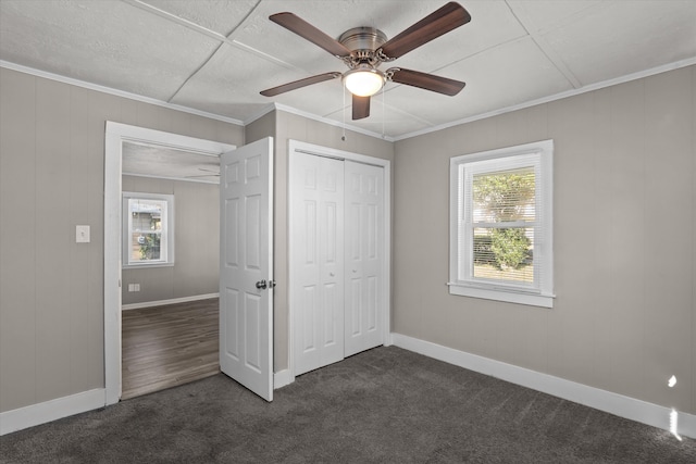 unfurnished bedroom with ceiling fan, dark carpet, ornamental molding, and a closet