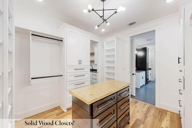 walk in closet featuring light wood-type flooring and a notable chandelier