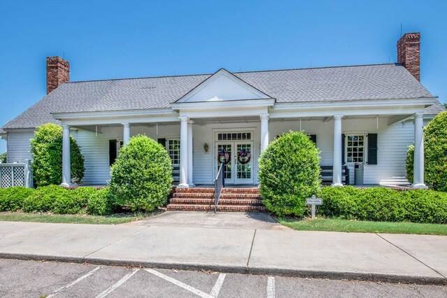 greek revival house with a chimney, roof with shingles, french doors, uncovered parking, and a porch