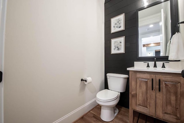 half bath with baseboards, vanity, toilet, and wood finished floors