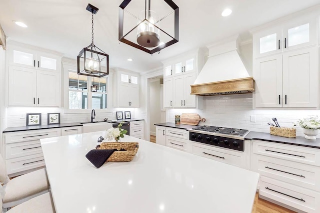 kitchen featuring stainless steel gas cooktop, a sink, white cabinetry, a center island, and custom range hood