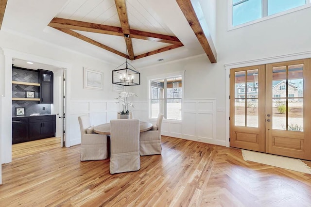 dining space featuring a decorative wall, french doors, wainscoting, beamed ceiling, and an inviting chandelier