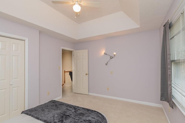 carpeted bedroom with a raised ceiling and ceiling fan