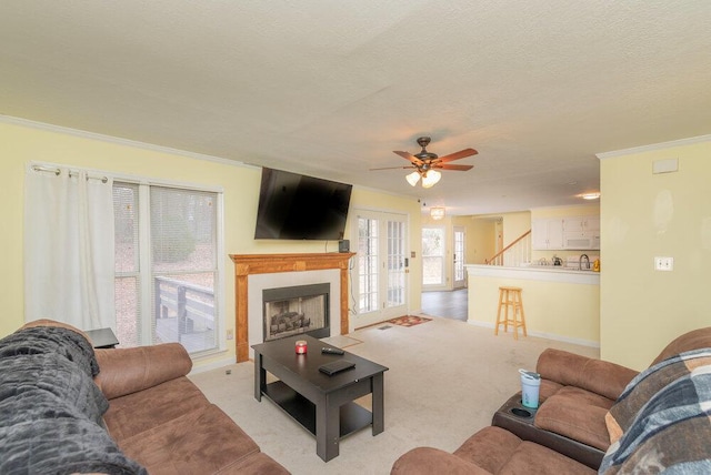 living room with ceiling fan, light colored carpet, ornamental molding, and a textured ceiling