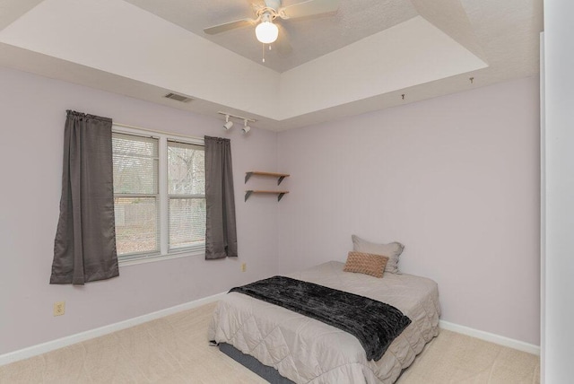 carpeted bedroom with a tray ceiling and ceiling fan