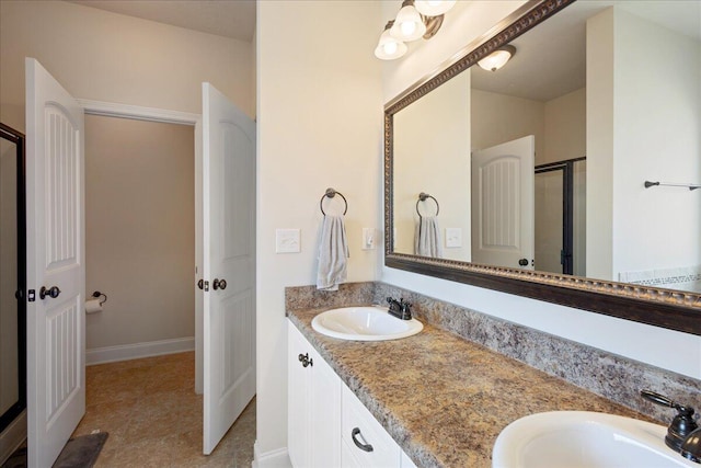 bathroom with double vanity, a stall shower, a sink, and baseboards