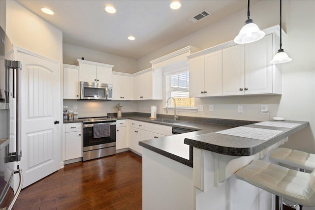 kitchen featuring stainless steel appliances, dark countertops, white cabinetry, a sink, and a peninsula