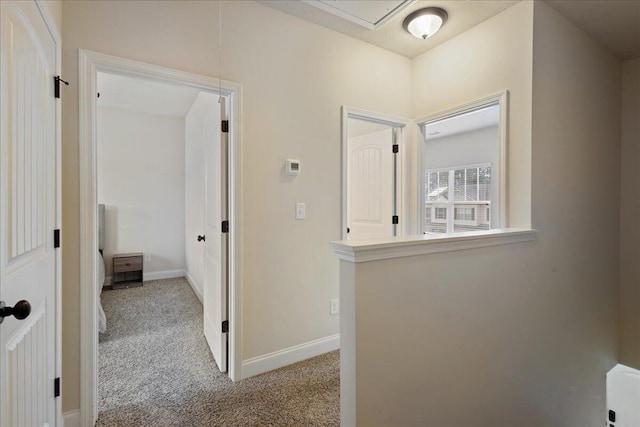 hall with carpet floors, attic access, and baseboards