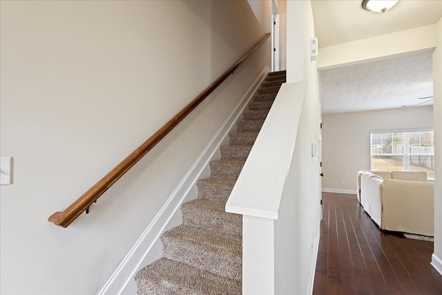 stairway with a textured ceiling, wood finished floors, and baseboards