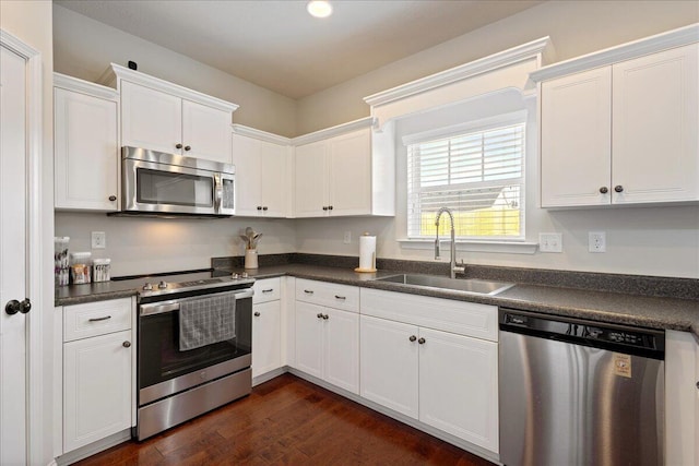 kitchen with stainless steel appliances, dark wood-style flooring, a sink, white cabinets, and dark countertops