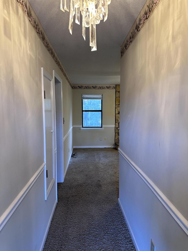 hall with dark carpet, a textured ceiling, and a chandelier