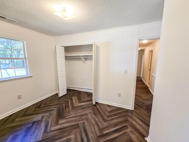 unfurnished bedroom featuring dark parquet flooring, a textured ceiling, a closet, and crown molding