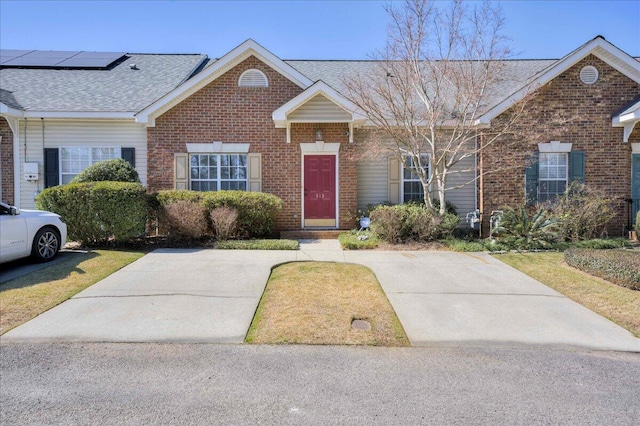 single story home with a front yard, a shingled roof, roof mounted solar panels, and brick siding