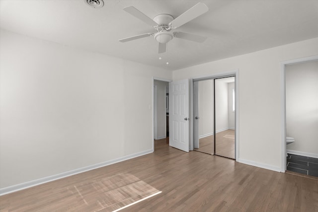 unfurnished bedroom with ceiling fan, wood-type flooring, ensuite bathroom, and a closet