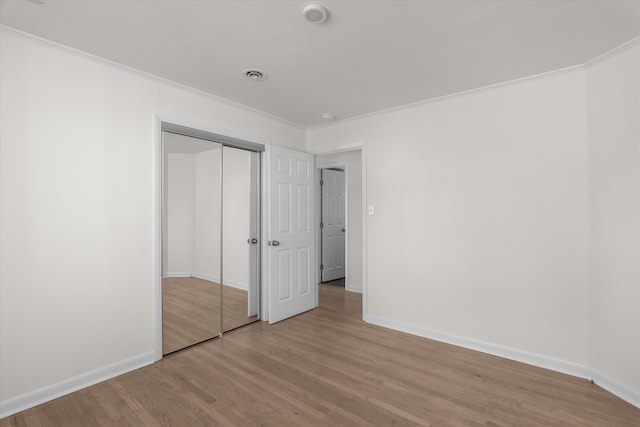 unfurnished bedroom featuring crown molding, light wood-type flooring, and a closet