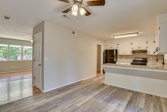 kitchen featuring light stone countertops, refrigerator, tasteful backsplash, black range with electric stovetop, and white cabinetry