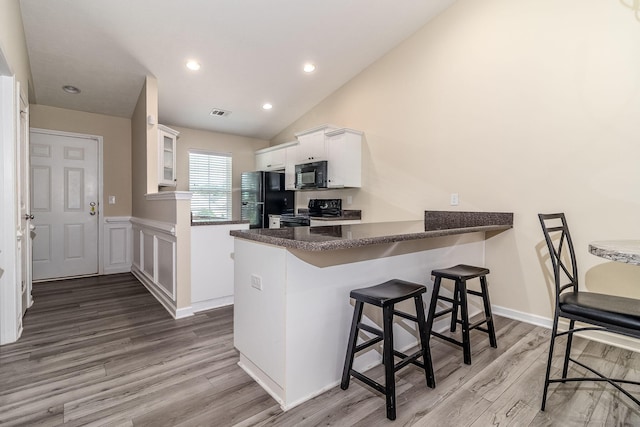 2697 York Dr, Augusta, GA 30909 - kitchen with black appliances, a peninsula, white cabinets, wood finished floors, and a breakfast bar