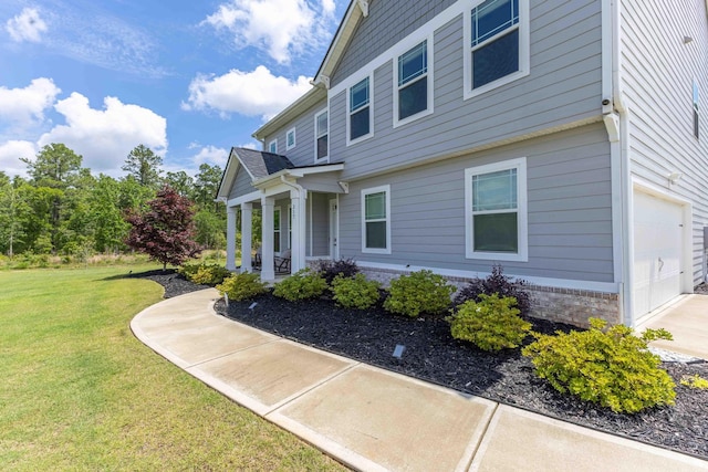 view of property exterior with a yard, covered porch, an attached garage, and driveway