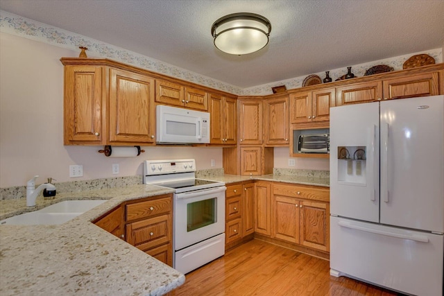 kitchen featuring a textured ceiling, light stone counters, white appliances, and sink