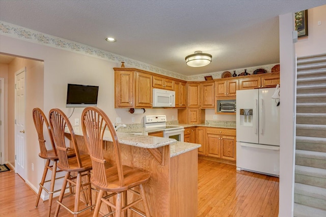 kitchen featuring a kitchen bar, white appliances, kitchen peninsula, and light hardwood / wood-style flooring