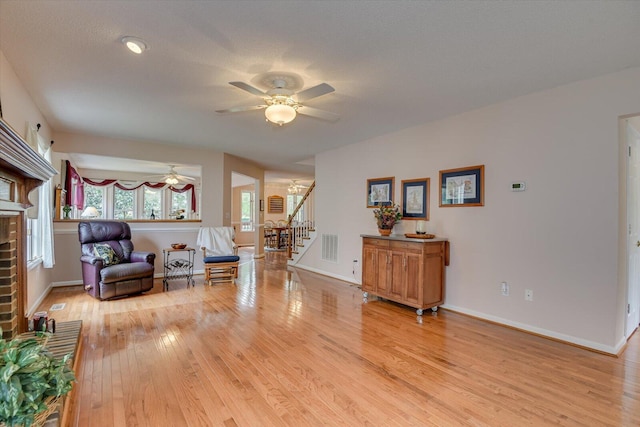 living area with a textured ceiling, light hardwood / wood-style flooring, a brick fireplace, and ceiling fan