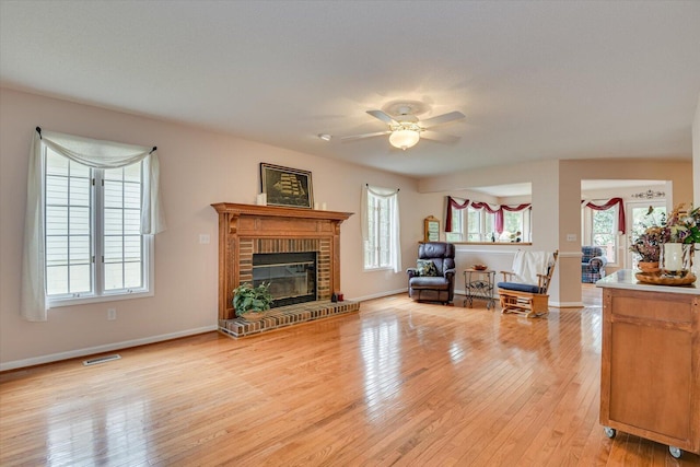 living room featuring light hardwood / wood-style floors, a brick fireplace, and ceiling fan