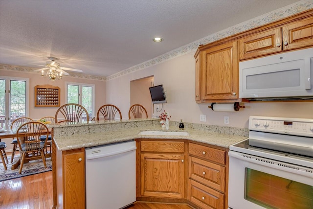 kitchen with white appliances, sink, light hardwood / wood-style flooring, ceiling fan, and kitchen peninsula