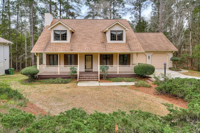 new england style home with covered porch, a garage, and a front lawn