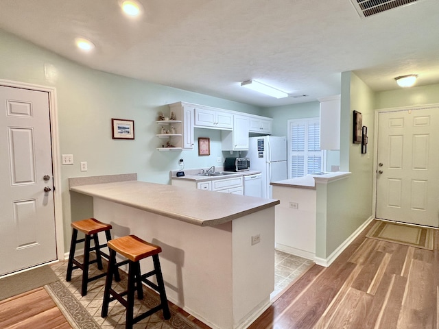 kitchen featuring a breakfast bar, white appliances, kitchen peninsula, sink, and white cabinetry