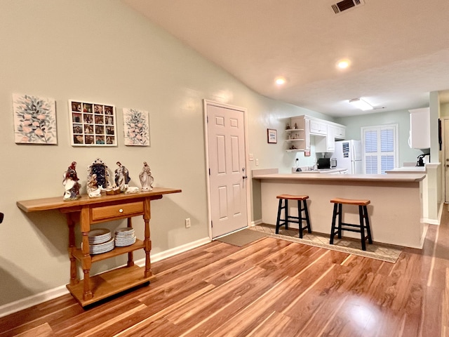 kitchen featuring a kitchen bar, kitchen peninsula, light hardwood / wood-style floors, white cabinets, and white fridge