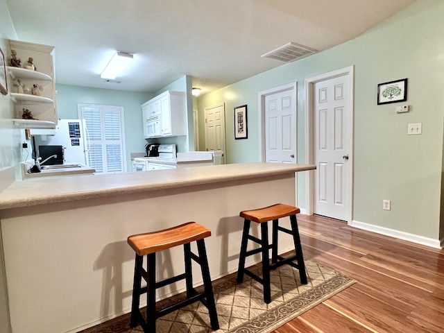 kitchen with a kitchen breakfast bar, kitchen peninsula, hardwood / wood-style floors, white appliances, and white cabinets