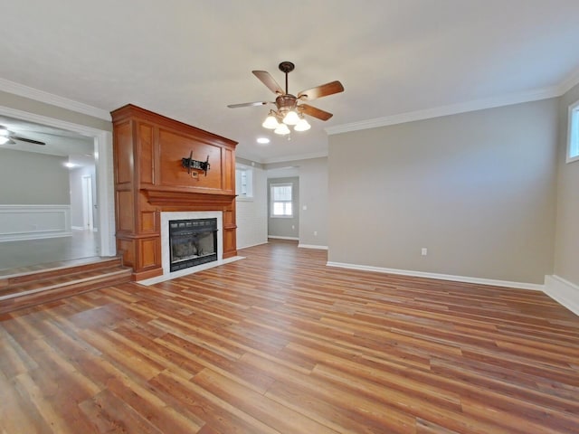 unfurnished living room with crown molding, a large fireplace, ceiling fan, and light wood-type flooring