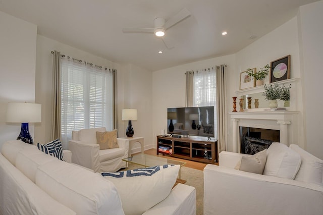 living room with a high end fireplace, wood-type flooring, ceiling fan, and a healthy amount of sunlight