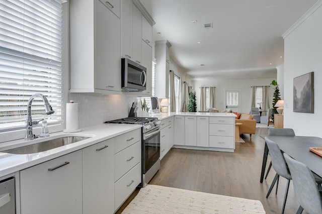 kitchen featuring sink, backsplash, kitchen peninsula, light hardwood / wood-style floors, and appliances with stainless steel finishes