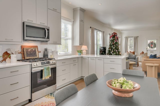 kitchen with kitchen peninsula, light wood-type flooring, decorative backsplash, appliances with stainless steel finishes, and ornamental molding